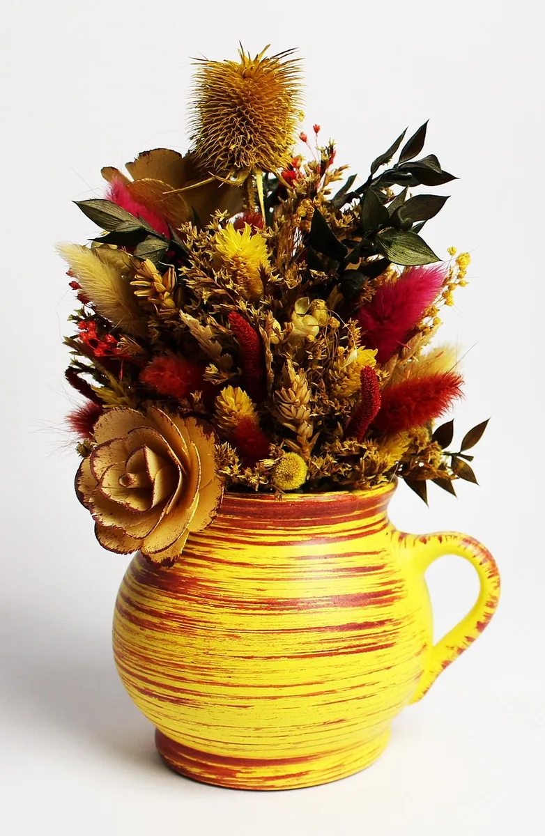 Trockenblumen und Gräser in einem gelben Keramikkrug